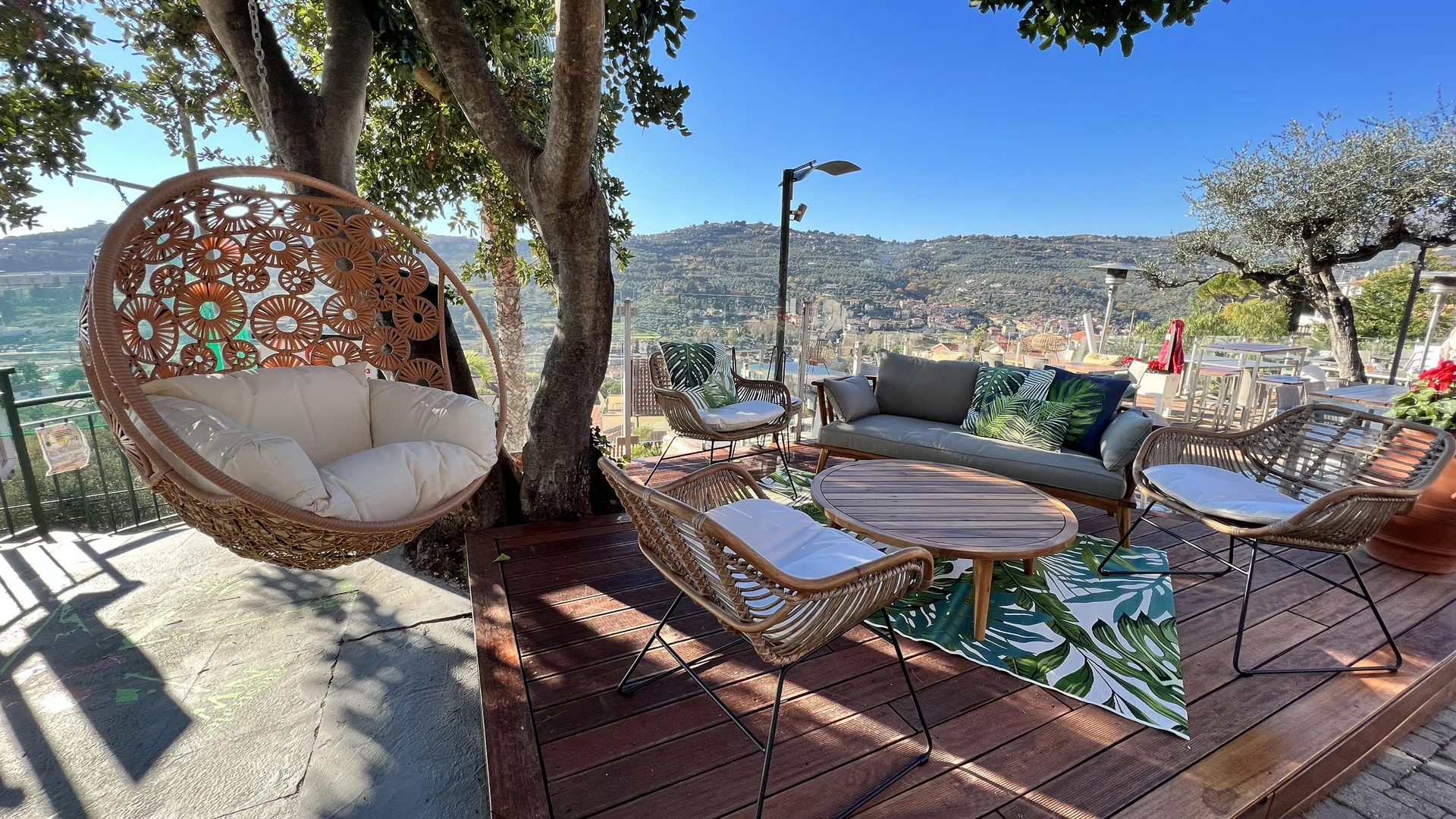Cozy outdoor seating area with wicker chairs and hanging chair on terrace with mountain view