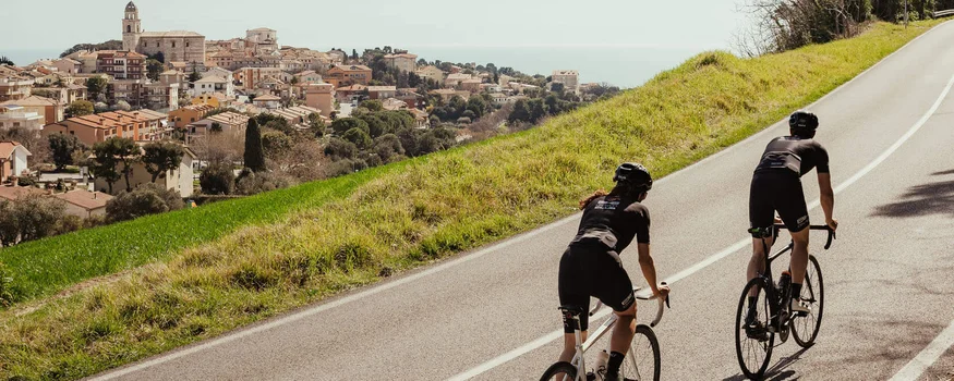 Zwei Radfahrer fahren bergauf auf einer Landstraße mit Stadt im Hintergrund
