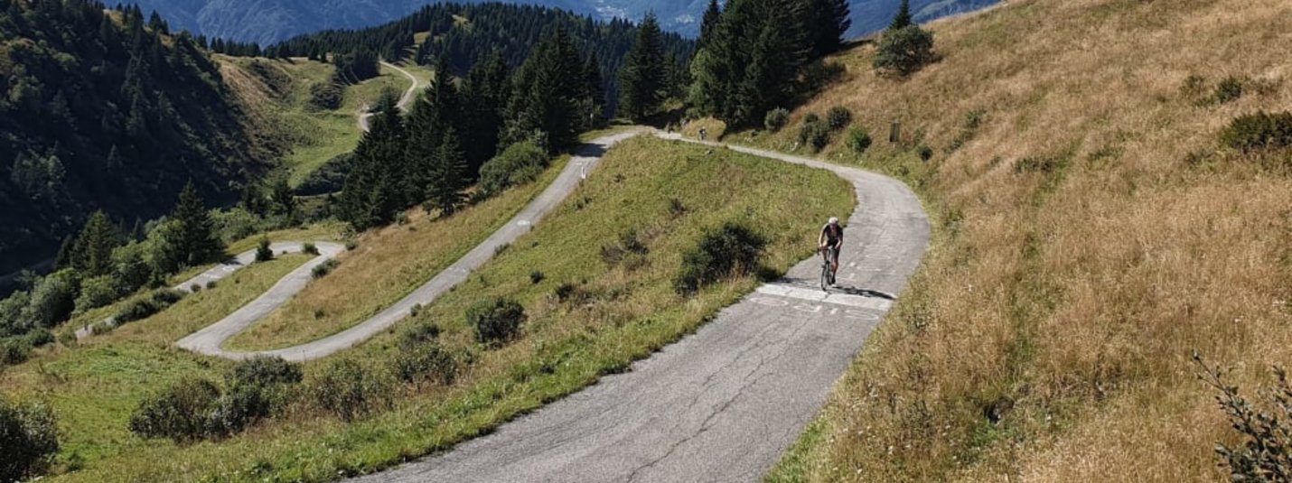 Ciclista su strada di montagna tortuosa con Alpi sullo sfondo
