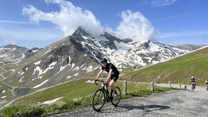 29. Glocknerkönig am 7. Juni 2026 © Tourismusverband BRUCK FUSCH GROSSGLOCKNER Radfahrer auf Bergstraße vor schneebedeckten Gipfeln und blauem Himmel