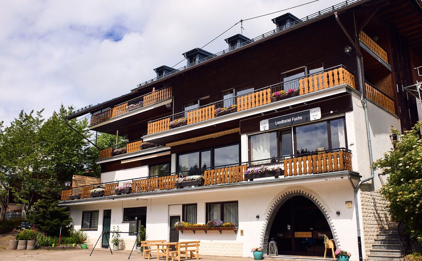 Landhotel mit Holzbalkonen und Blumendekoration an sonnigem Tag