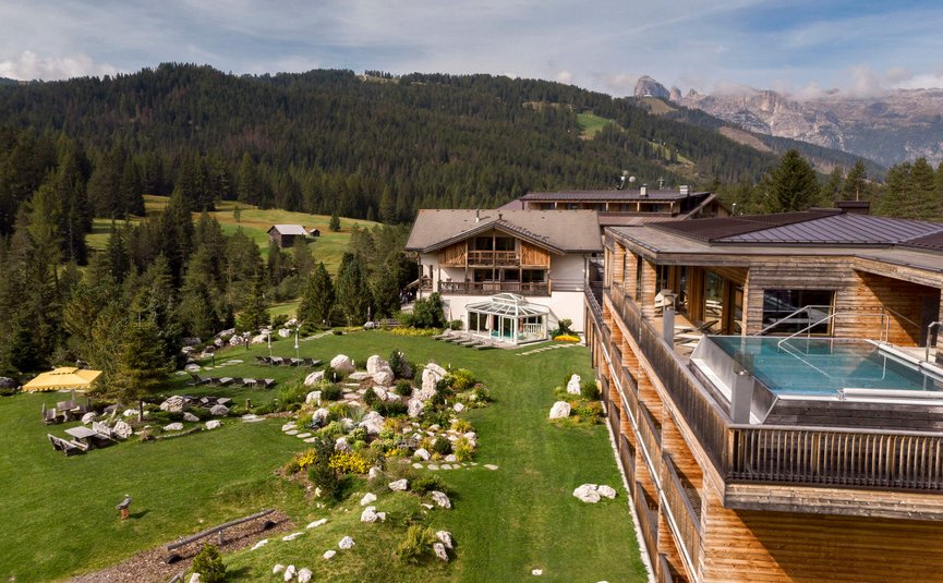 Hotel mit Außenpool auf Terrasse und grüner Wiese vor Bergwald