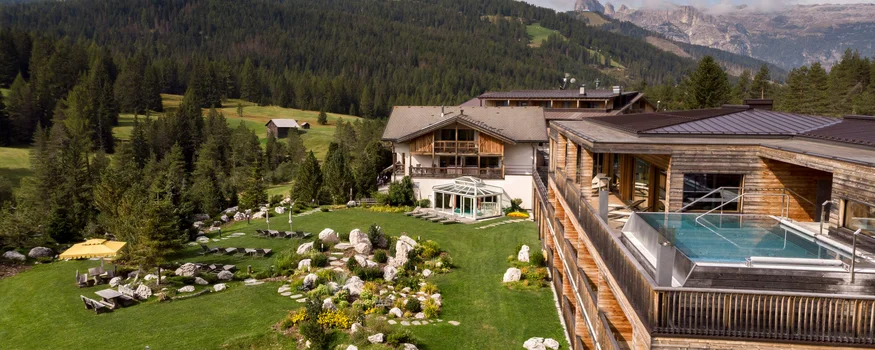 Hotel with outdoor pool, green lawn, and forested mountains in the background