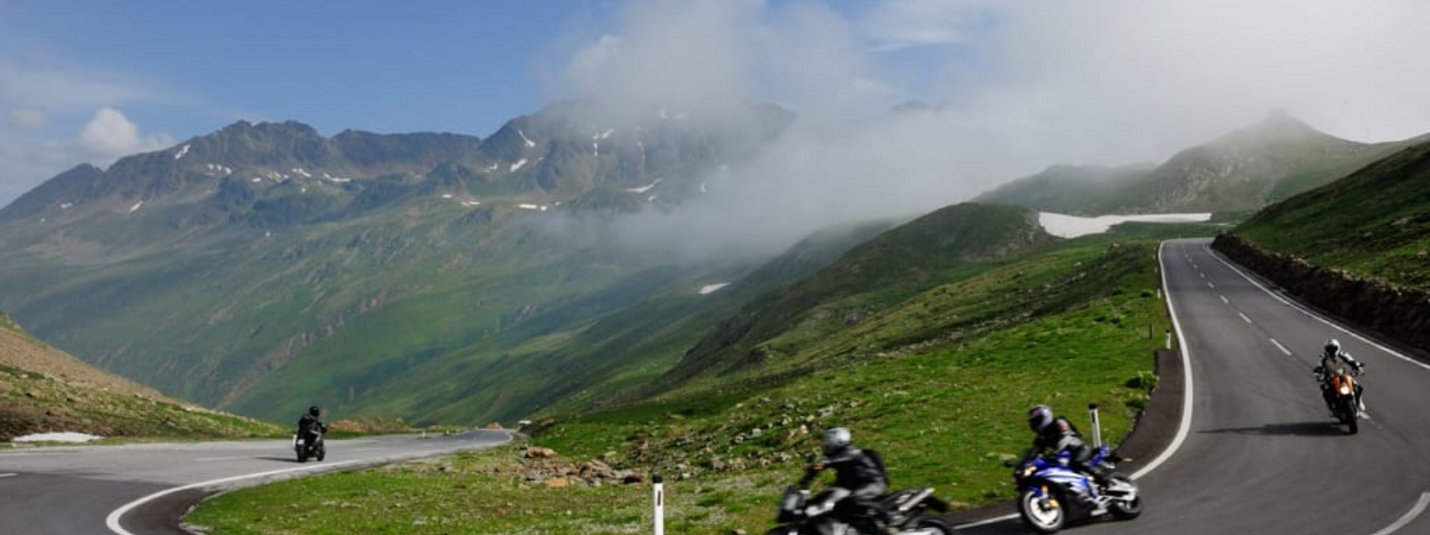 Motociclisti su strada di montagna tortuosa sotto cielo nuvoloso