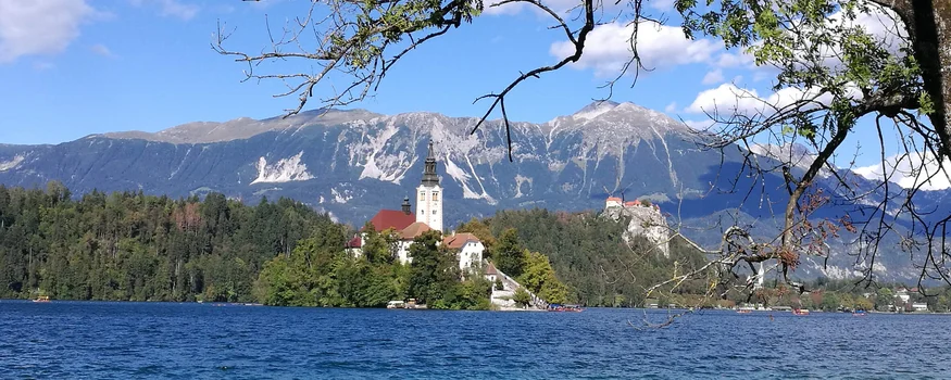 Hotel & Glamping Ribno Alpine Resort **** © Epidos doo Kirche auf einer Insel im See vor Bergen bei klarem Himmel