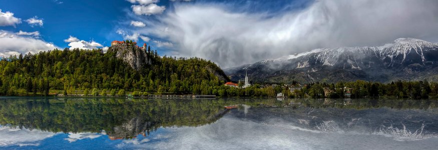 Castello su collina boschiva con lago e montagne innevate sullo sfondo