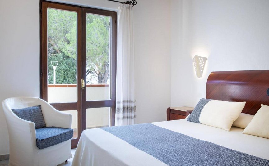 Bright bedroom with double bed, armchair, and balcony overlooking trees