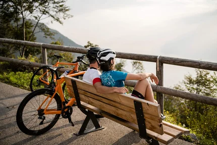 Coppia con casco da bici seduta su panchina con vista paesaggio