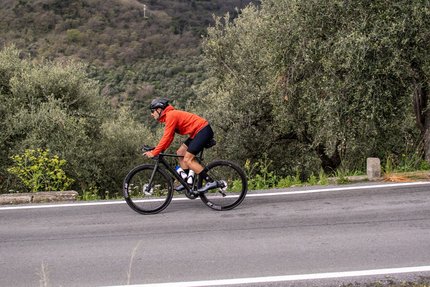 Cyclist in red jacket riding on mountain road near olive trees