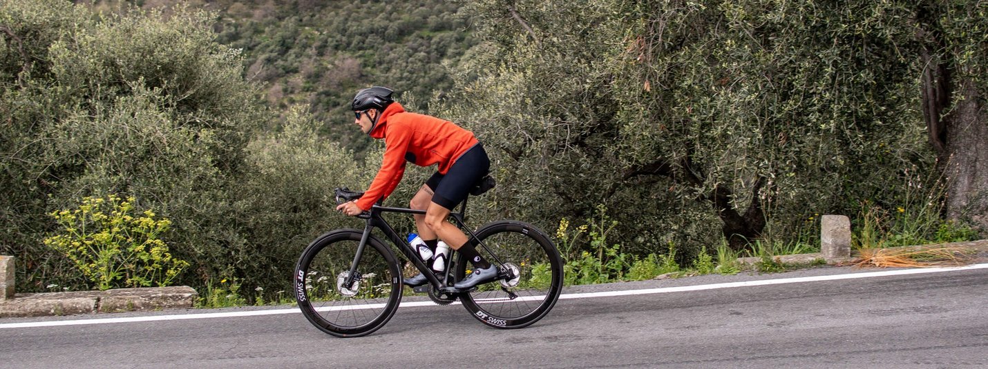 Ciclista con giacca rossa su strada di montagna vicino a ulivi