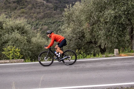 Fietser in rode jas op bergweg langs olijfbomen