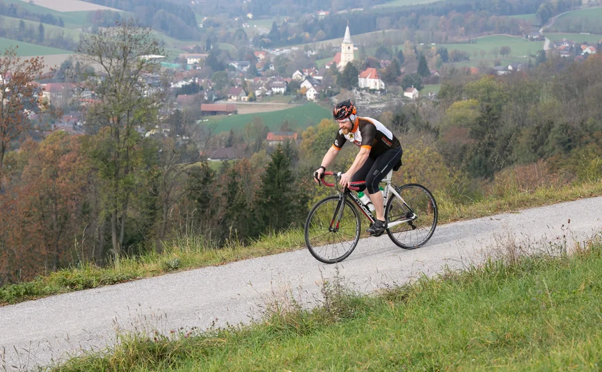 Ciclista su strada di campagna con villaggio e colline sullo sfondo