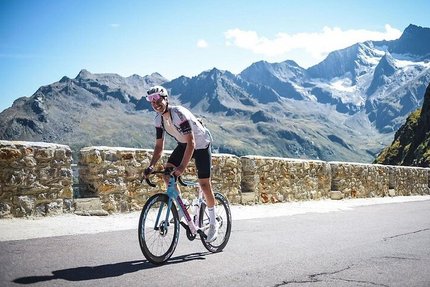 Radfahrer auf Bergstraße mit Steinmauer und Alpen im Hintergrund