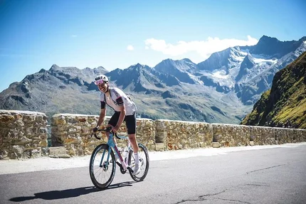 Fietser op bergweg met stenen muur en Alpen op de achtergrond