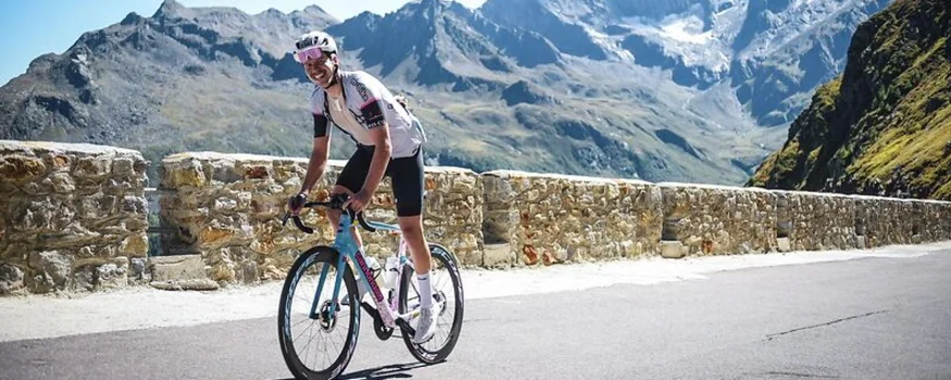 Radfahrer auf Bergstraße mit Steinmauer und Alpen im Hintergrund