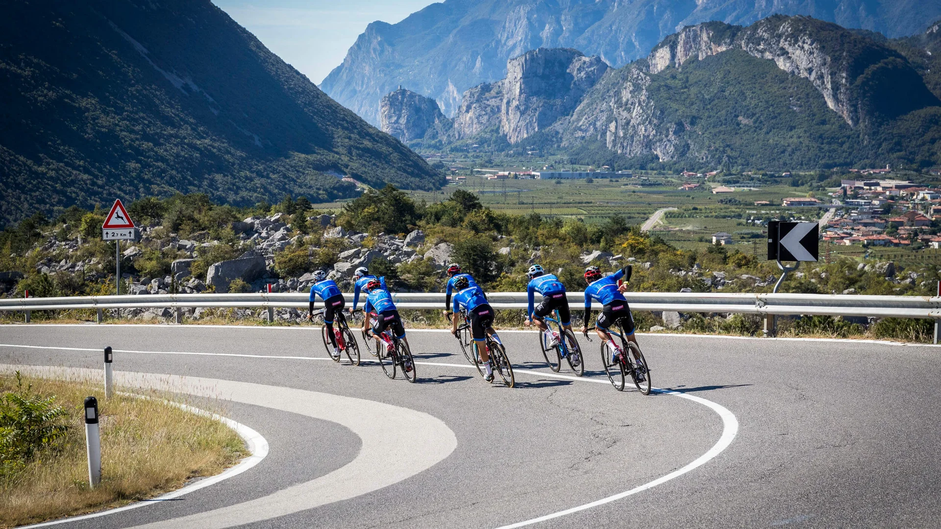 Six cyclists riding on a mountain road with mountains in the background