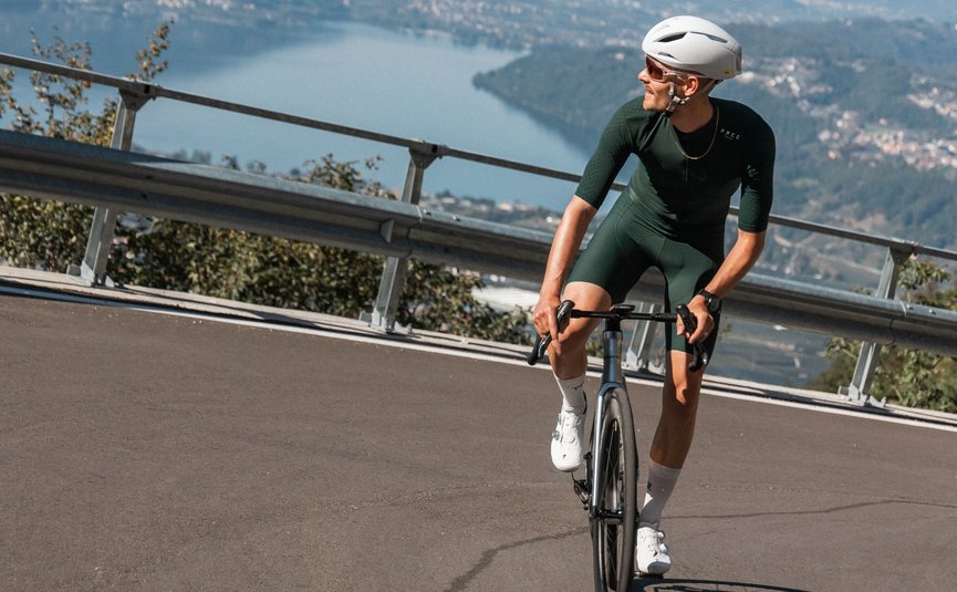 Ciclista con abbigliamento verde su strada di montagna con lago e montagne sullo sfondo