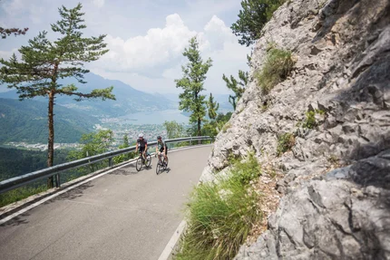Twee fietsers rijden op bergweg met uitzicht op meer en bergen