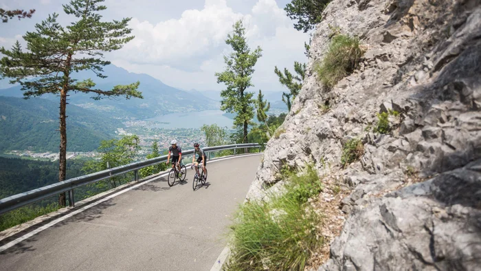 Zwei Radfahrer fahren auf einer Bergstraße mit Blick auf See und Berge