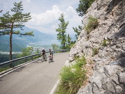 Zwei Radfahrer fahren auf einer Bergstraße mit Blick auf See und Berge