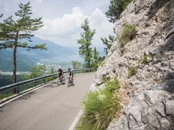 Zwei Radfahrer fahren auf einer Bergstraße mit Blick auf See und Berge