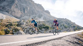 Due ciclisti pedalano su una strada di montagna con il sole