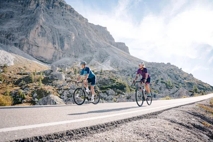 Two cyclists riding on a mountain road in sunny weather