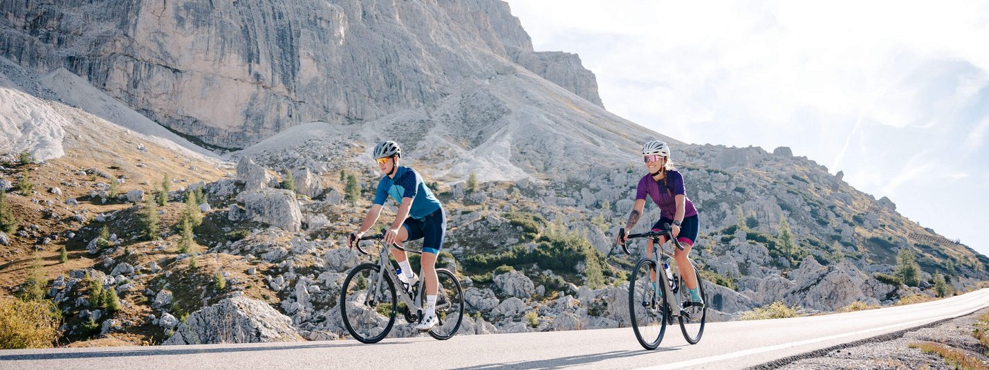 Due ciclisti pedalano su una strada di montagna con il sole