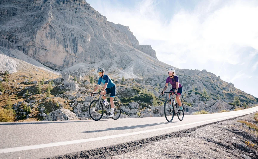 Due ciclisti pedalano su una strada di montagna con il sole