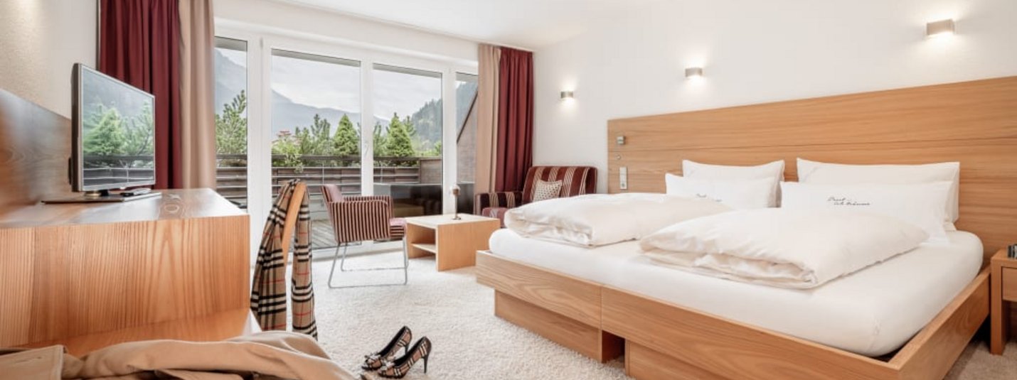 Camera d'albergo luminosa con letto matrimoniale, balcone e vista montagna