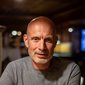 Older man with gray beard and t-shirt sitting at a table