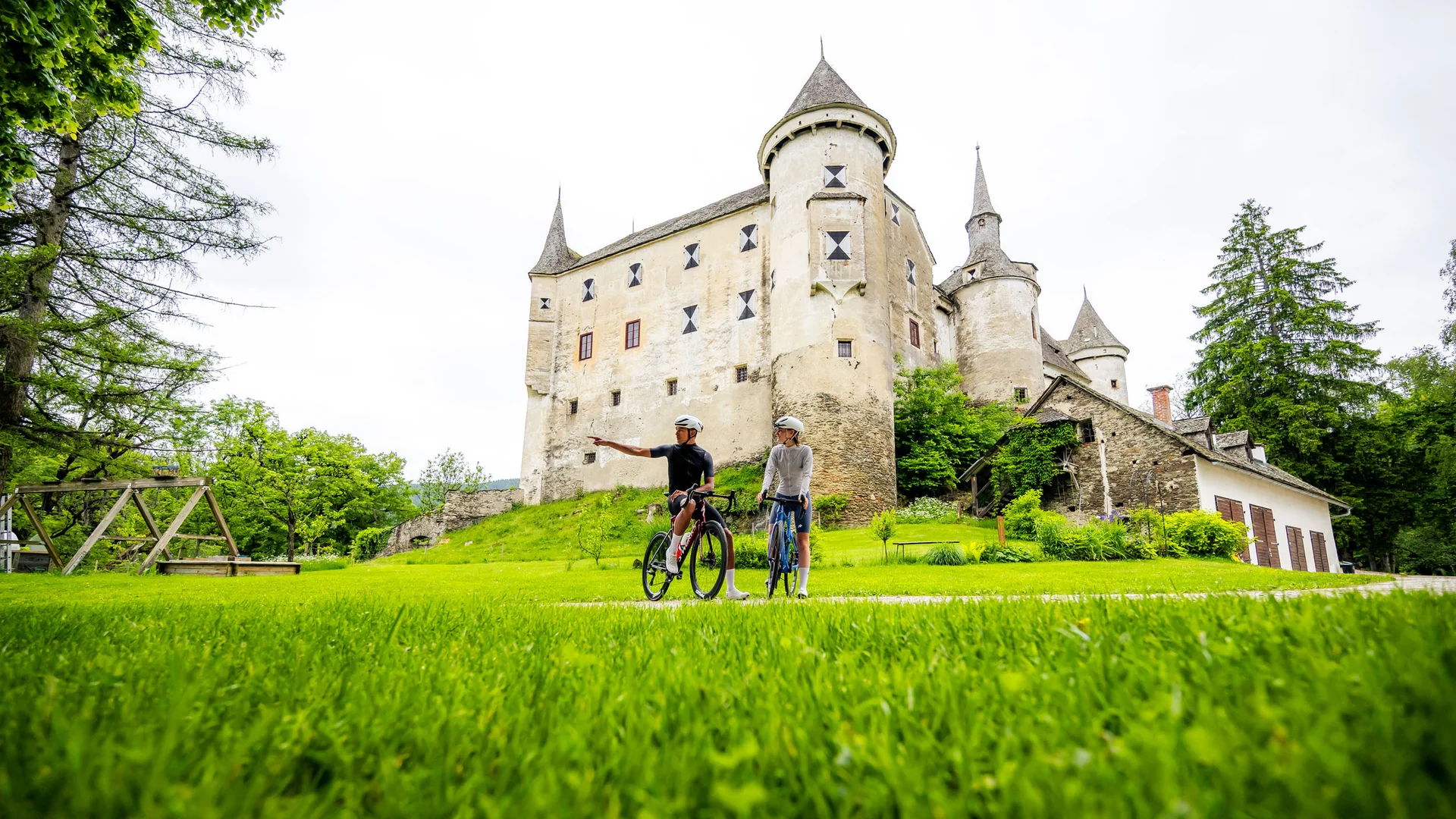 Two cyclists in front of a historic castle in a green landscape