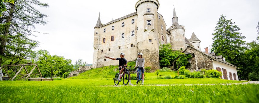 Two cyclists in front of a historic castle in a green landscape