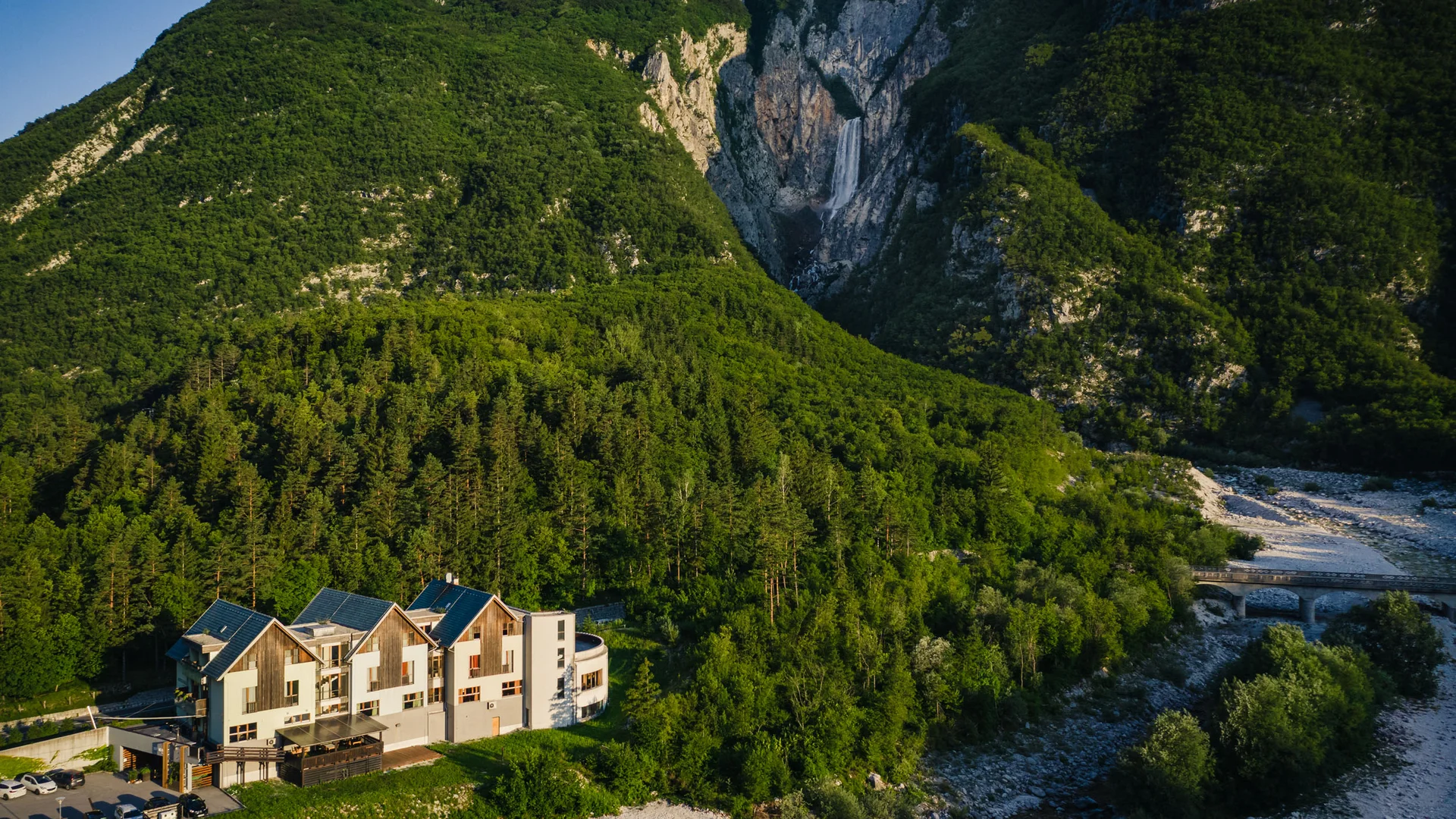 Haus vor bewaldeten Bergen und Wasserfall im Tal
