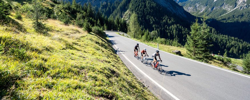 Erlebe den Tannheimer Tal Radmarathon 2024 © Christina Neubauer Drei Radfahrer auf Bergstraße umgeben von Bergen und grünem Gras