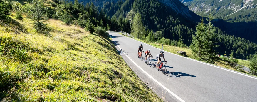 Drei Radfahrer auf Bergstraße umgeben von Bergen und grünem Gras
