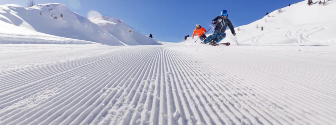 Zwei Skifahrer fahren auf einer frisch präparierten Piste im sonnigen Winter