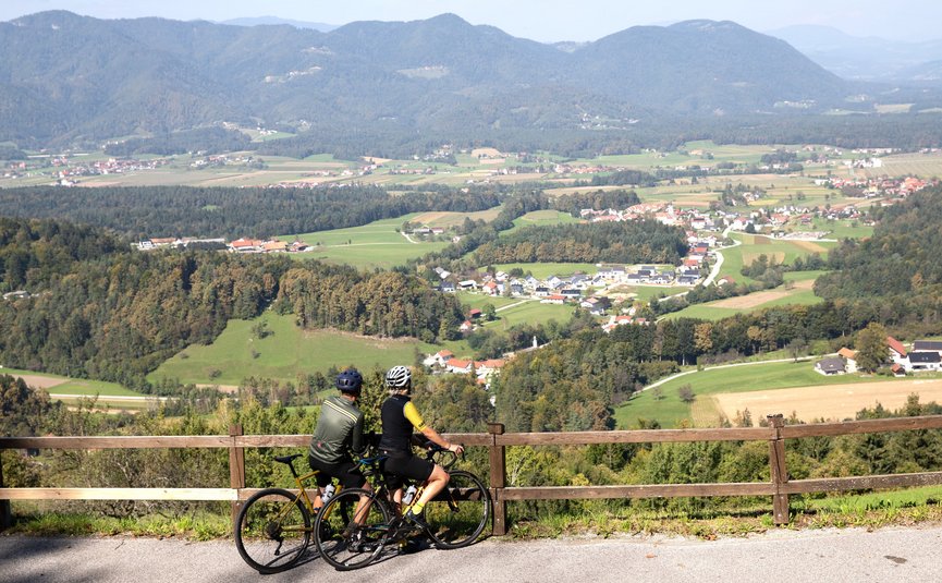 Due ciclisti guardano un villaggio e montagne in una valle soleggiata