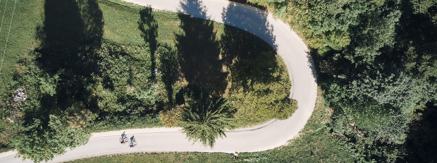 Luftaufnahme von zwei Radfahrern auf geschwungener Straße durch grüne Landschaft