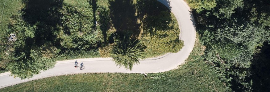 Aerial view of two cyclists on a curved road through green landscape