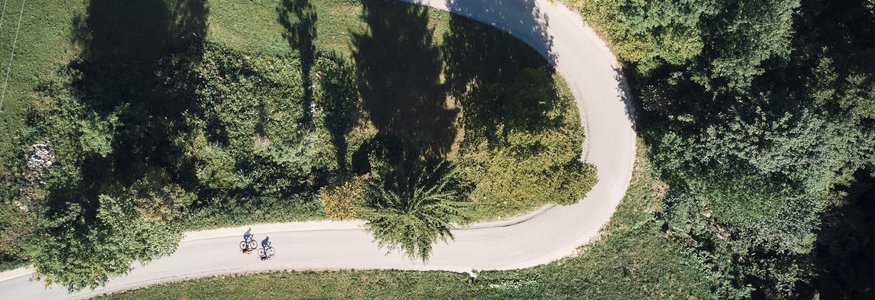 Luftaufnahme von zwei Radfahrern auf geschwungener Straße durch grüne Landschaft