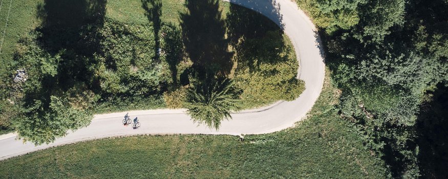 Bayerischer Wald © Tobias Köhler Luftaufnahme von zwei Radfahrern auf geschwungener Straße durch grüne Landschaft