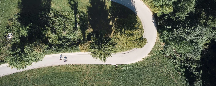 Luftaufnahme von zwei Radfahrern auf geschwungener Straße durch grüne Landschaft