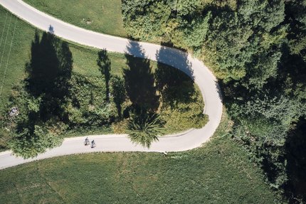 Luftaufnahme von zwei Radfahrern auf geschwungener Straße durch grüne Landschaft