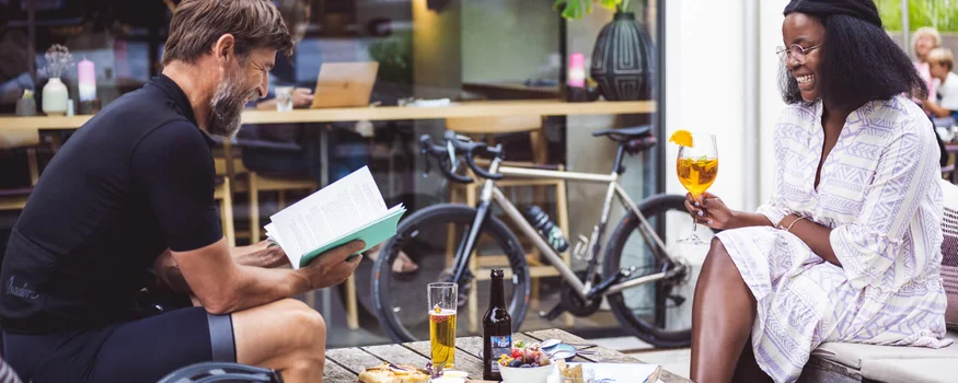 A racing bike weekend in the Bregenzerwald © Stefan Leitner Man reading book and woman holding drink at café with bicycle in background