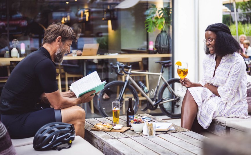 Man reading book and woman holding drink at café with bicycle in background