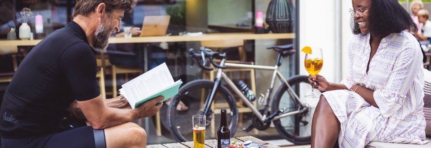 Mann liest Buch, Frau hält Getränk, Fahrrad im Hintergrund in Café