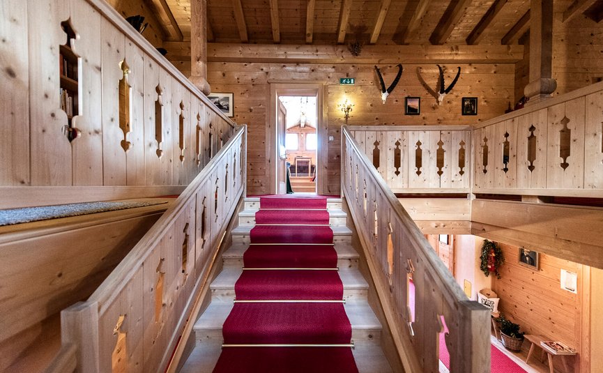 Holztreppe mit rotem Teppich in einem traditionellen Chalet mit Geweih an der Wand