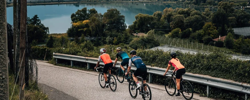 5 Rennrad-Highlights in Tramin © Jens Scheibe Vier Radfahrer fahren auf einer Straße neben einem See und Bergen