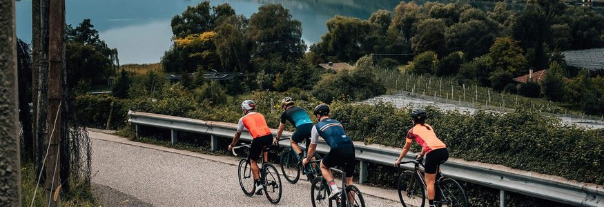 Vier Radfahrer fahren auf einer Straße neben einem See und Bergen